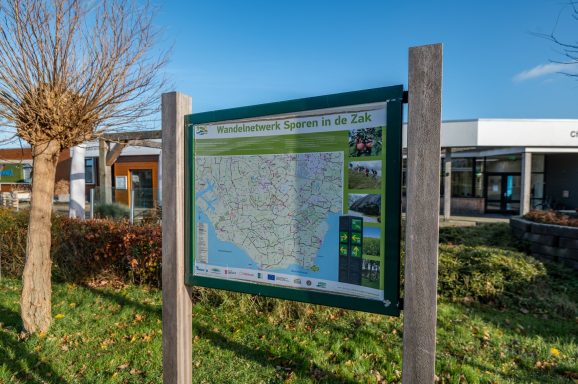 Informatiebord met een kaart en richtingen, omgeven door gras en bomen.