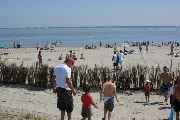 Kinderen en volwassenen genieten van een zonnig strand met veel mensen en parasols.