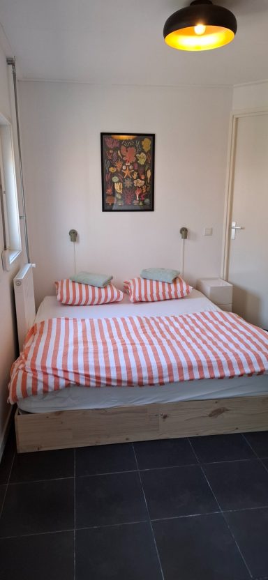 Sfeervolle slaapkamer met een tweepersoonsbed en vrolijk beddengoed met gestreept dessin.