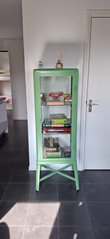 Groene vitrinekast met boeken en spelletjes.