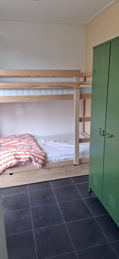 Een eenvoudige kamer met een stapelbed, een bed en een groene kast.