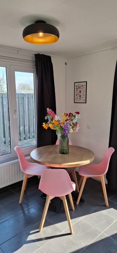 Ronde tafel met bloemenvaas en roze stoelen in een moderne, lichte eetruimte.