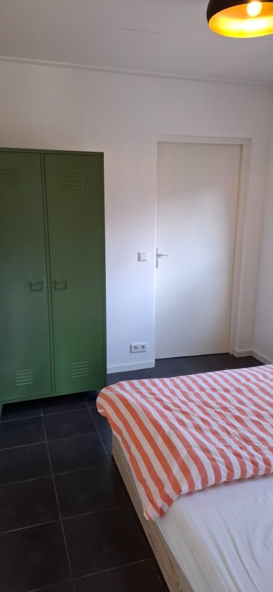 Sfeervolle slaapkamer met een bed en een groene kast tegen een lichte muur.