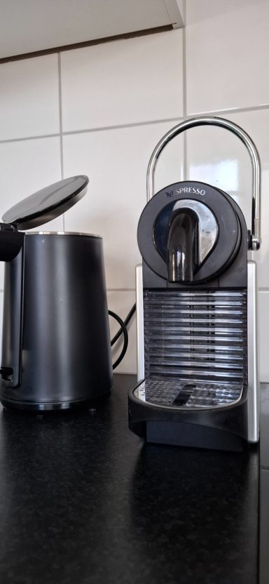 Zwarte Nespresso-machine naast een waterkoker op een zwart aanrecht.