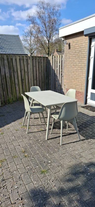 Tuinset met een tafel en vier stoelen op een steenslagterras, achter een schutting.