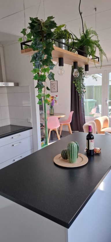 Moderne keuken met zwart aanrecht, planken met planten en een houten serveerbord.