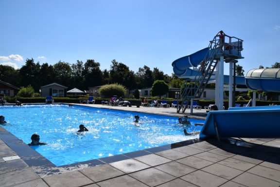 Zwemmen in een buitenzwembad met een glijbaan en een duikplank in de zon.