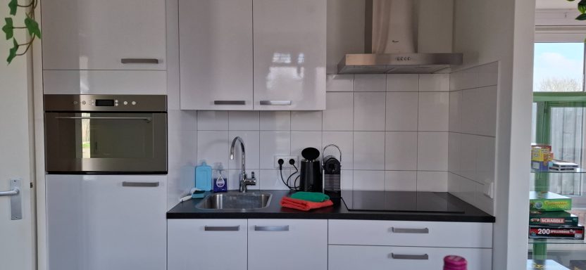Moderne keuken met witte kasten, een oven, gootsteen en koffiezetapparaat.